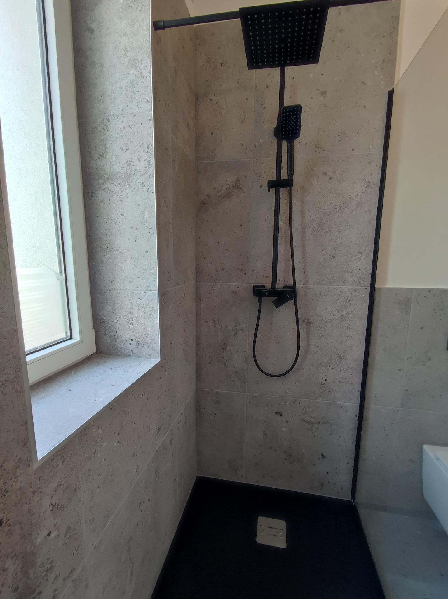 Wykończona kabina prysznicowa z czarną armaturą i szarymi płytkami imitującymi kamień, widok z niskiej perspektywy na czarny brodzik.