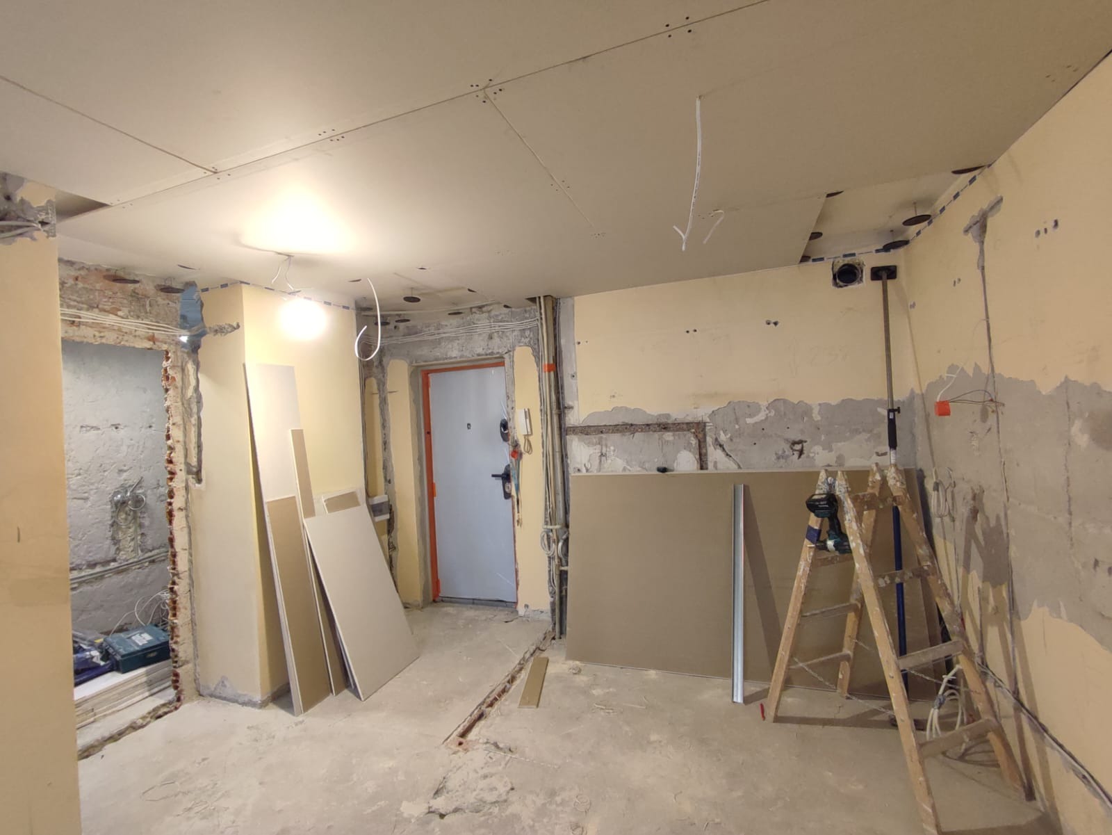 Wnętrze w trakcie remontu z częściowo zamontowanymi płytami karton-gips na suficie, odsłoniętymi fragmentami ścian, stojącymi arkuszami płyt, drabiną i narzędziami.