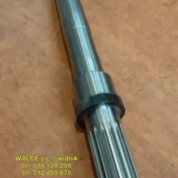 Metalowy wał z frezowanymi rowkami, widoczne ślady obr&oacute;bki, obok naklejka z logo firmy WALCE s.c. Świdnik i danymi kontaktowymi.