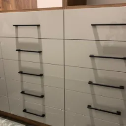 Szare, lakierowane fronty szafy wnękowej z poziomymi, czarnymi uchwytami, widoczny fragment drewnianej obudowy u góry i marmurowa posadzka u dołu.