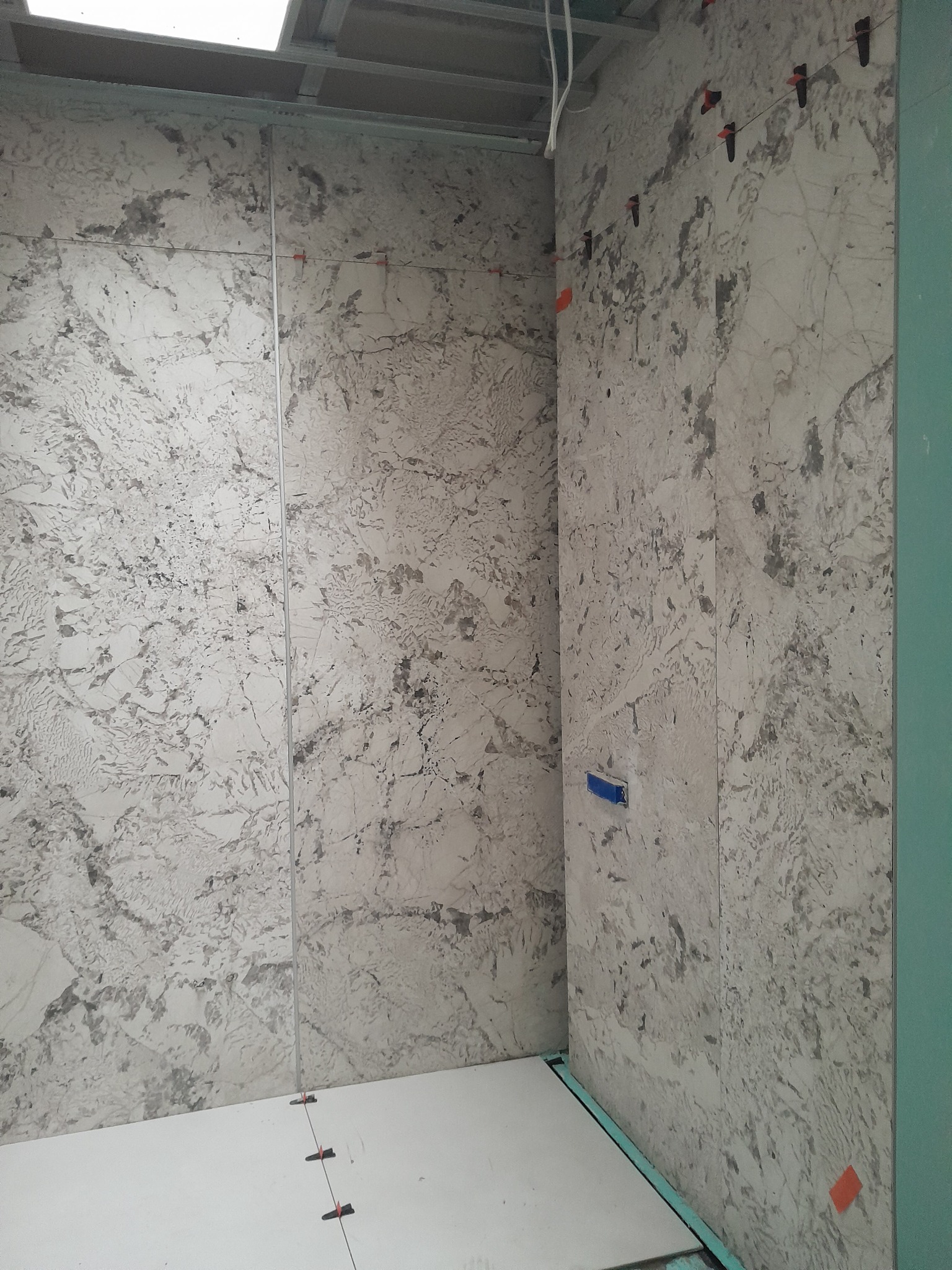 Montaż dużych płyt imitujących marmur na ścianach w trakcie prac wykończeniowych, widoczne klipsy poziomujące i niebieska taśma maskująca.