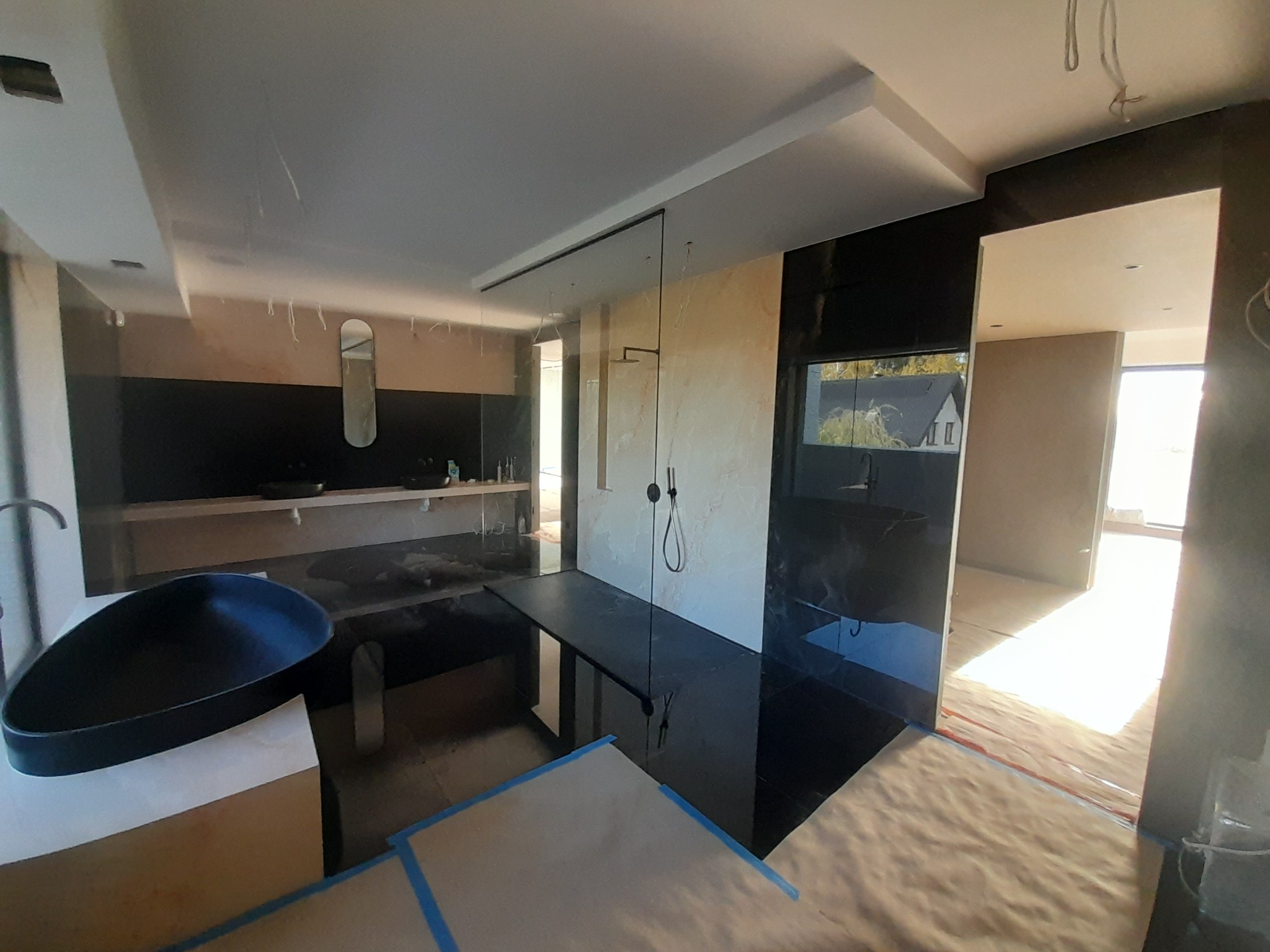 Nowoczesna łazienka w trakcie wykańczania, z czarną armaturą, kabiną prysznicową typu walk-in i przygotowanym podłożem pod posadzkę.