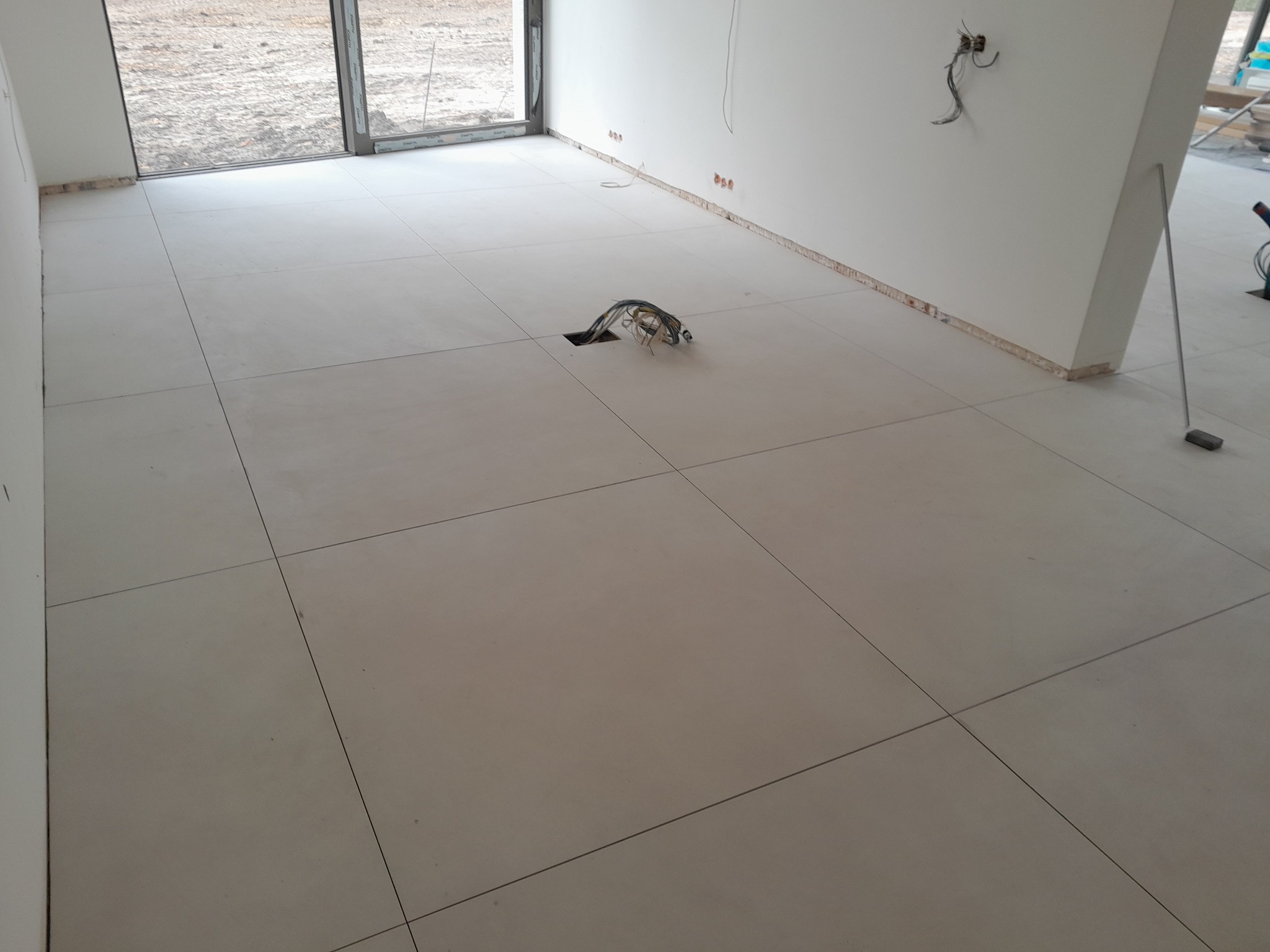 Ułożone jasne płytki podłogowe z widocznym otworem na kable elektryczne w nowym pomieszczeniu w trakcie wykańczania.