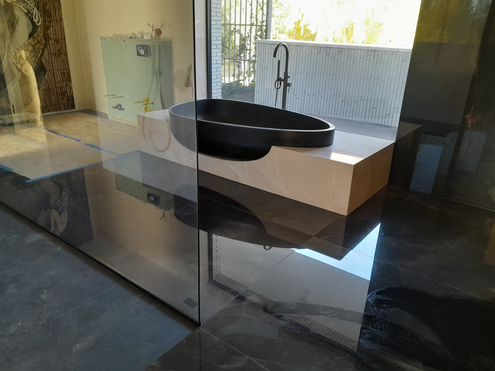 Nowoczesna czarna wanna wolnostojąca na marmurowym podeście, widoczna przez szklaną ścianę, z czarną armaturą i odbiciem w polerowanej podłodze