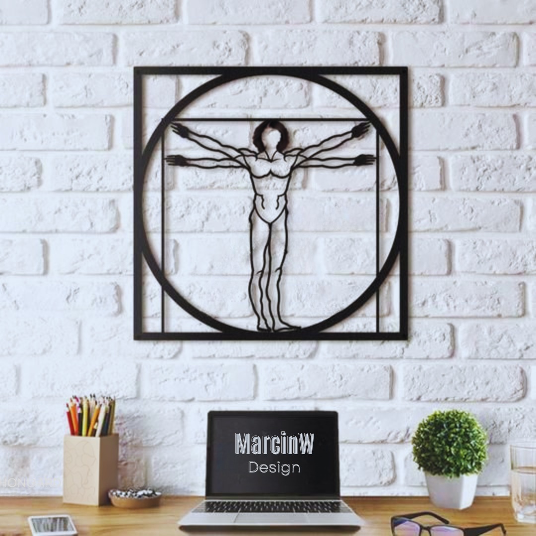 Metalowa dekoracja ścienna przedstawiająca Człowieka Witruwiańskiego na tle białej ściany z cegieł, poniżej biurko z laptopem z napisem 'MarcinW Design', obok doniczka z małą rośliną, ołówki...