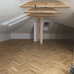 Perfect Wall - Poddasze po remoncie z nową podłogą ułożoną w jodełkę, drewnianymi elementami dekoracyjnymi na suficie i oknem dachowym, ściany przygotowane do malowania.