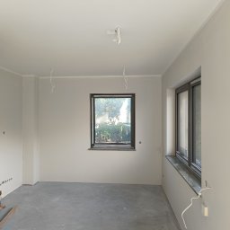 Perfect Wall - Wnętrze pokoju po szpachlowaniu ścian na gładko, z widocznym workiem zaprawy, przewodami elektrycznymi wystającymi ze ścian i sufitu oraz oknem z widokiem na zieleń.