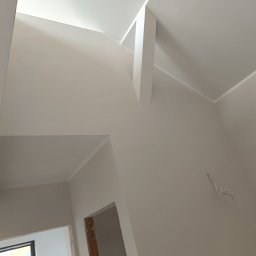 Perfect Wall - Wysoki sufit pod skosem, świeżo pomalowany na jasny odcień beżu, widoczne listwy przypodłogowe i wystający fragment ściany, surowe kable elektryczne wystające ze ściany.
