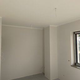 Perfect Wall - Jasne, świeżo pomalowane wnętrze pokoju z oknem, widoczne wystające kable elektryczne i listwa przypodłogowa, ślady zabrudzeń na szybie okiennej.