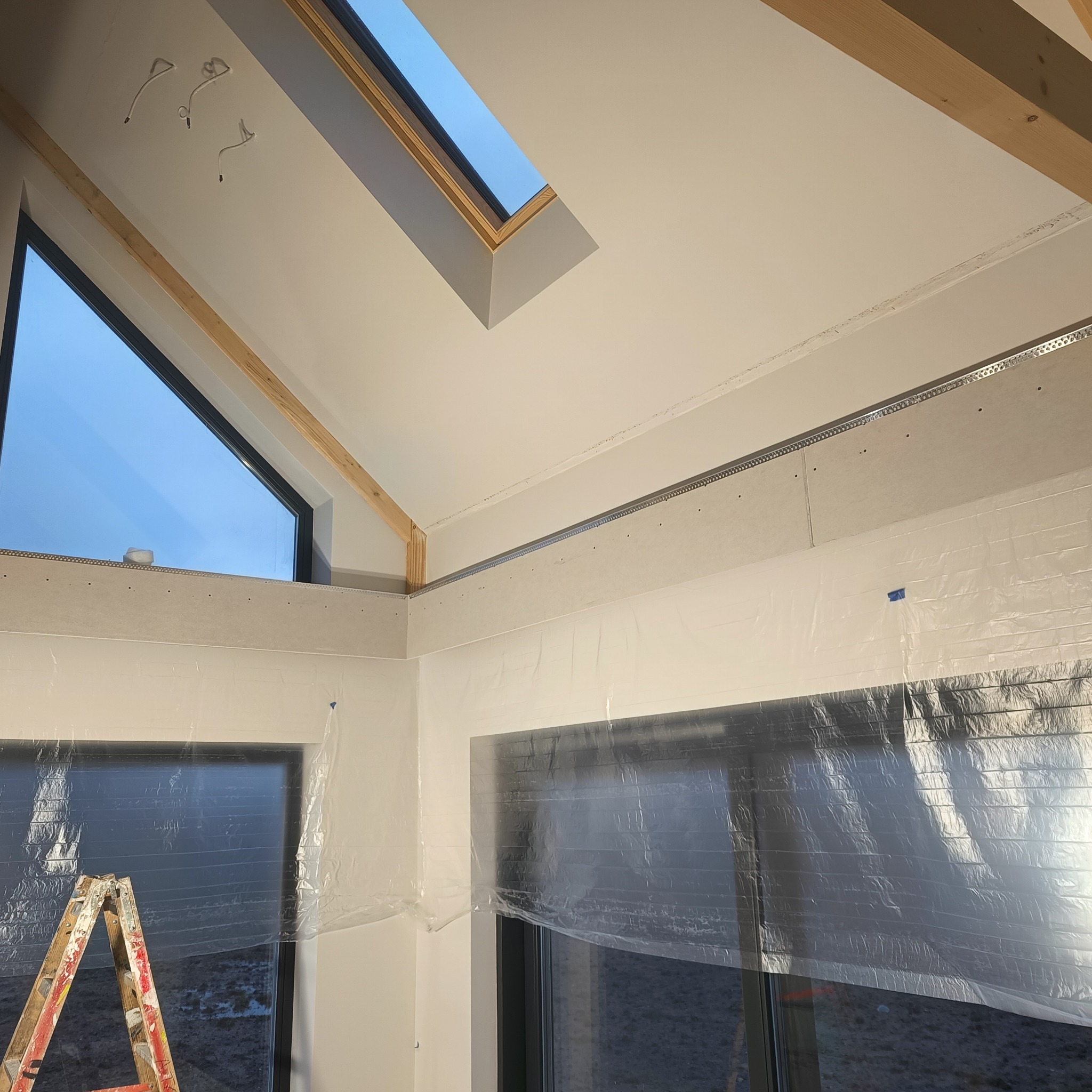Wnętrze w trakcie prac wykończeniowych: zamontowane płyty karton-gips na poddaszu, okna zabezpieczone folią malarską, widoczna drabina malarska.