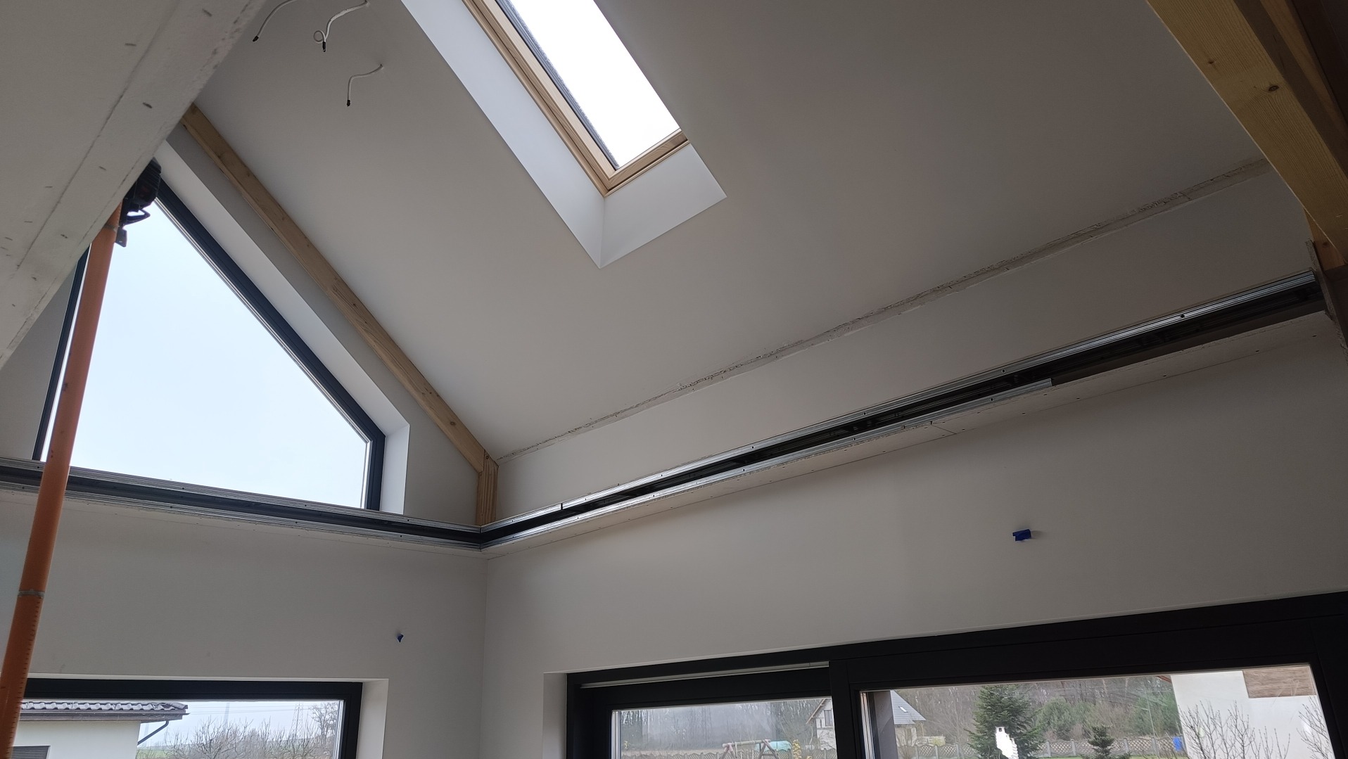 Wnętrze poddasza z oknami dachowymi i szkieletem metalowym pod zabudowę płytami gipsowo-kartonowymi, widoczne kable elektryczne i fragmenty konstrukcji drewnianej.