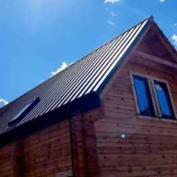 Nowoczesny dom z bali z ciemnym, metalowym dachem na tle błękitnego nieba z chmurami.