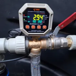 Manometr IBOpress 10-1/4 cala podłączony do instalacji wodnej z zaworem, wskazujący ciśnienie 2.94 bar, z widocznymi elementami złącznymi i przewodami z tworzywa sztucznego.