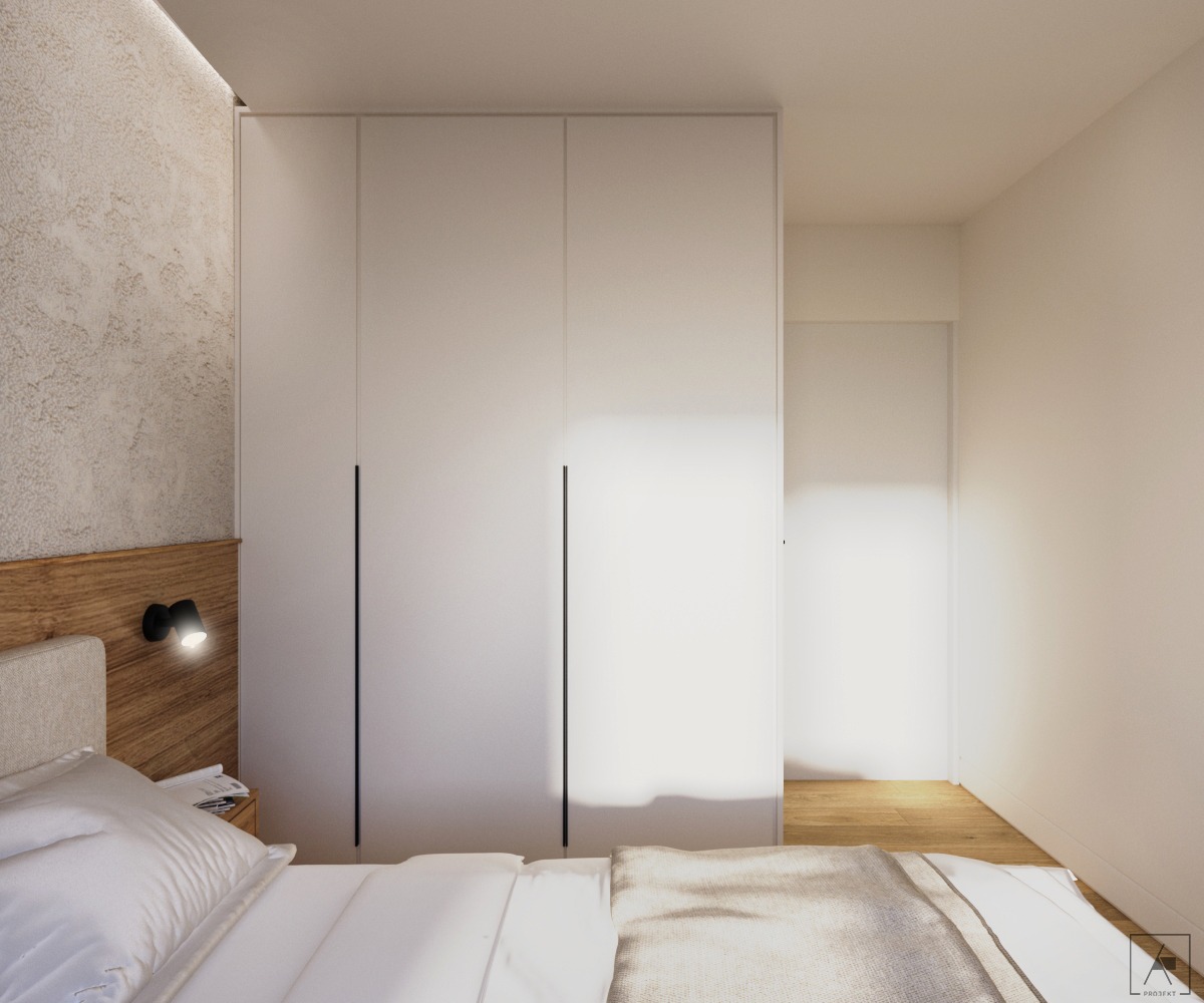 Minimalistyczna sypialnia z dużym, białym wbudowanym szafą, drewnianym zagłówkiem i lampką nocną, widok na przejście do innego pomieszczenia z drewnianą podłogą.