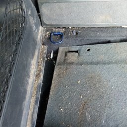 MARTOM Martyna LANGER - Brudny bagażnik samochodu z widoczną siatką, uchwytem mocującym i dywanikiem pokrytym okruchami i kurzem przed czyszczeniem.