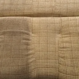 Zbliżenie na teksturowaną, beżową tapicerkę kanapy z widocznymi wgłębieniami po guzikach, ukazującą splot materiału.