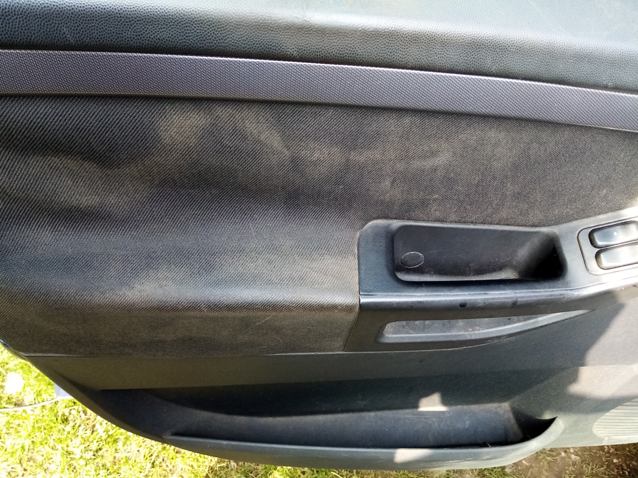 Wnętrze drzwi samochodu z widocznymi zabrudzeniami na tapicerce i plastikowych elementach, wymagające czyszczenia.