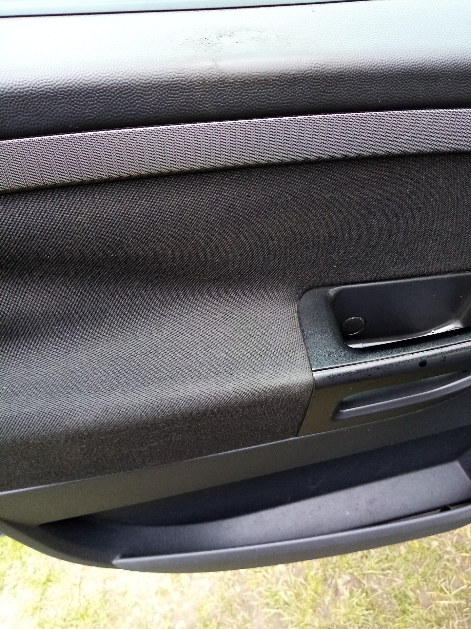 Wnętrze drzwi samochodu z tapicerowaną powierzchnią, widoczne ślady użytkowania i uchwyt.