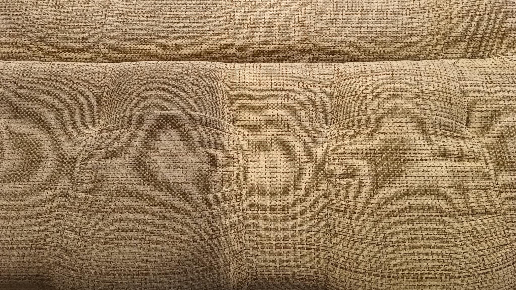 Zbliżenie na teksturowaną, beżową tapicerkę kanapy z widocznymi wgłębieniami po guzikach, ukazującą splot materiału.