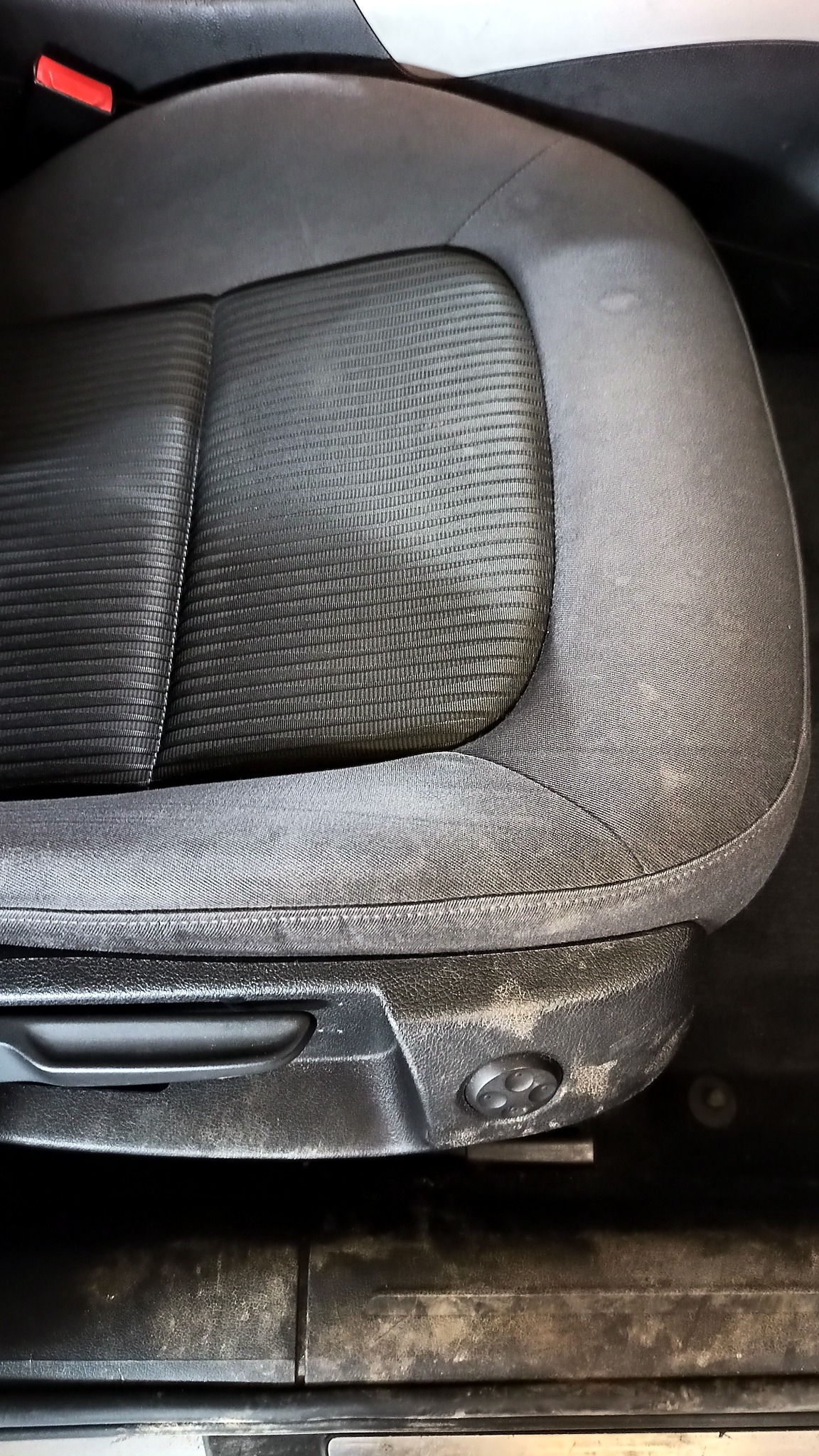 Brudny, szary fotel samochodowy z widocznymi plamami i zabrudzeniami na tapicerce, uchwycony z bliska.