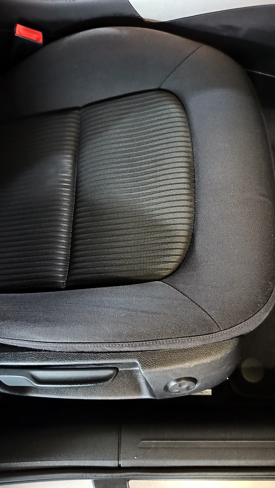 Czarne, tekstylne siedzenie samochodowe z widocznymi detalami faktury materiału i elementami regulacji.