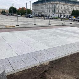 StarBRUK - Fragment placu miejskiego z nową, jasnoszarą nawierzchnią z kamiennych płyt, widoczne palety z materiałem i ogrodzenie budowy w tle.