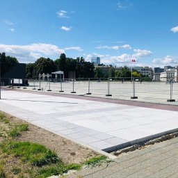 StarBRUK - Nowa, jasnoszara nawierzchnia placu miejskiego z kostki, oddzielona od trawnika szarym obrzeżem, w tle widoczne budynki miejskie i zabezpieczenia budowy.