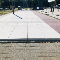 StarBRUK - Nowa, jasna nawierzchnia z dużych płyt na placu miejskim, widoczne prace wykończeniowe i ekipa w oddali, w tle zieleń miejska i budynek.