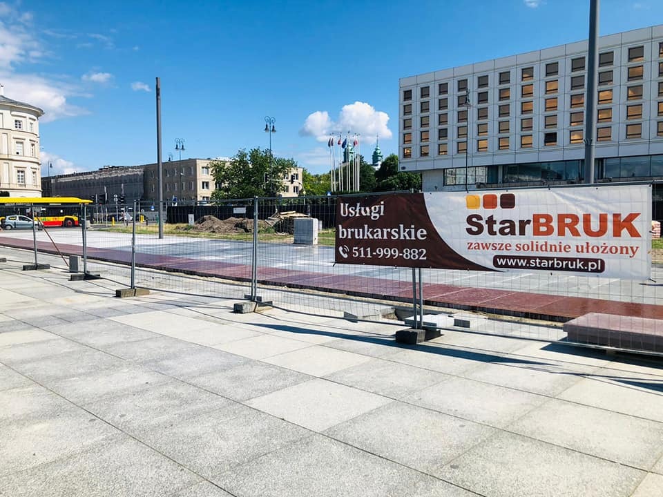 Baner reklamowy firmy StarBRUK z numerem telefonu na tle placu z nową nawierzchnią, zabezpieczonego metalowym ogrodzeniem tymczasowym.