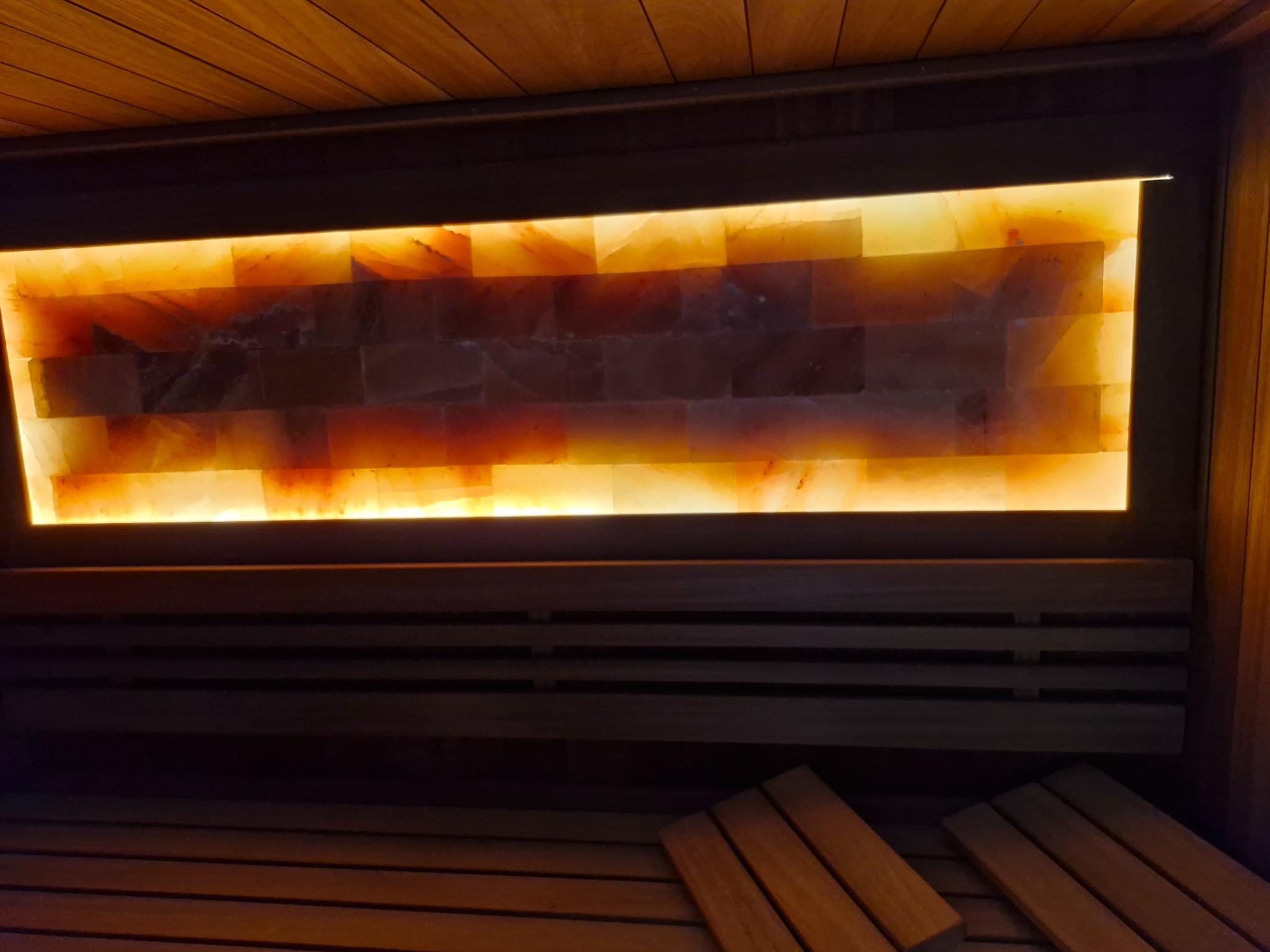 Wnętrze sauny z podświetlaną ścianą z cegieł solnych, drewniane ławki w ciepłym oświetleniu, widok z dołu.