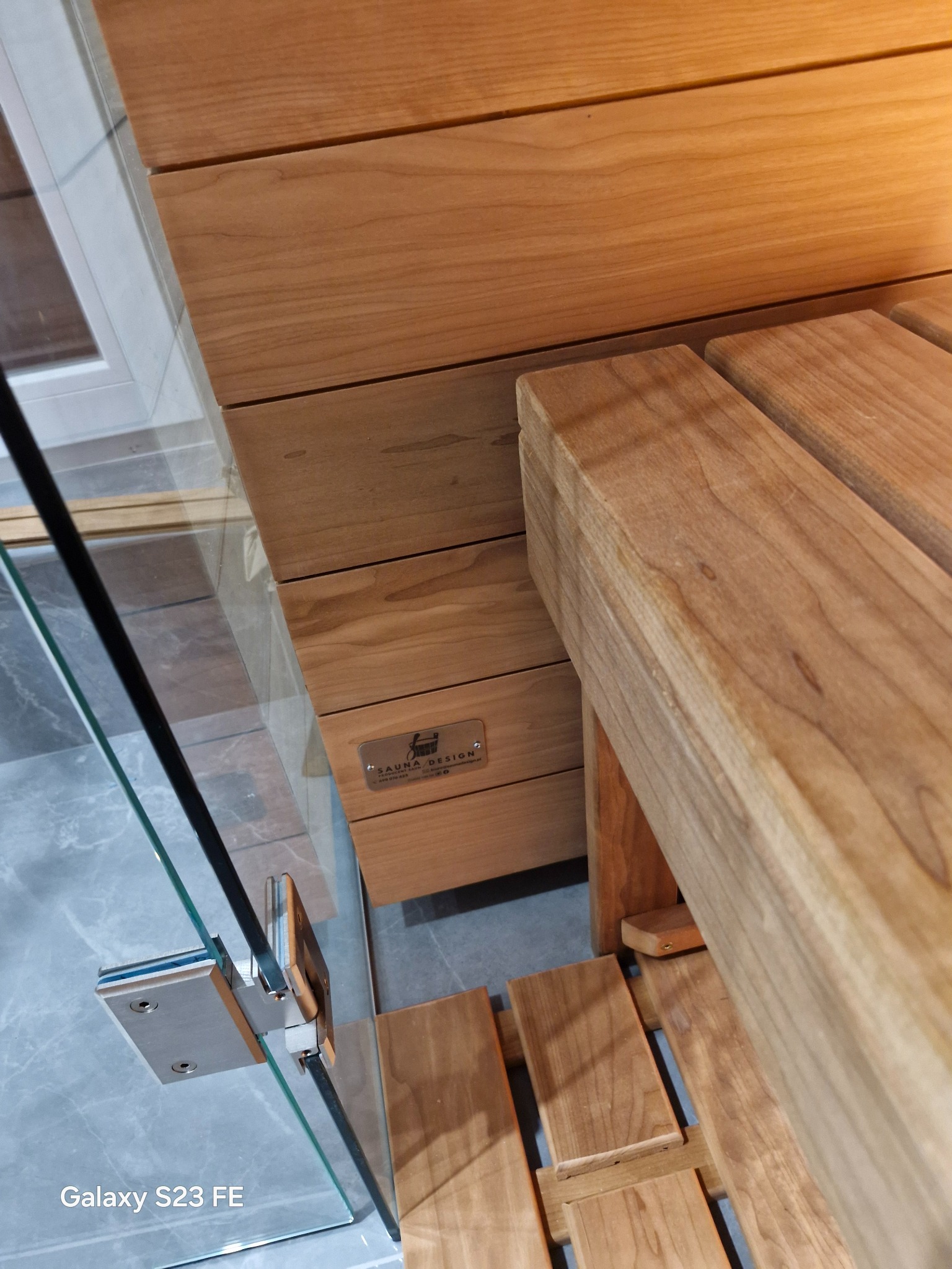 Szczegółowe ujęcie wnętrza sauny z drewnianymi ławkami i szklanymi drzwiami, ukazujące precyzję wykonania i dbałość o detale wykończenia.