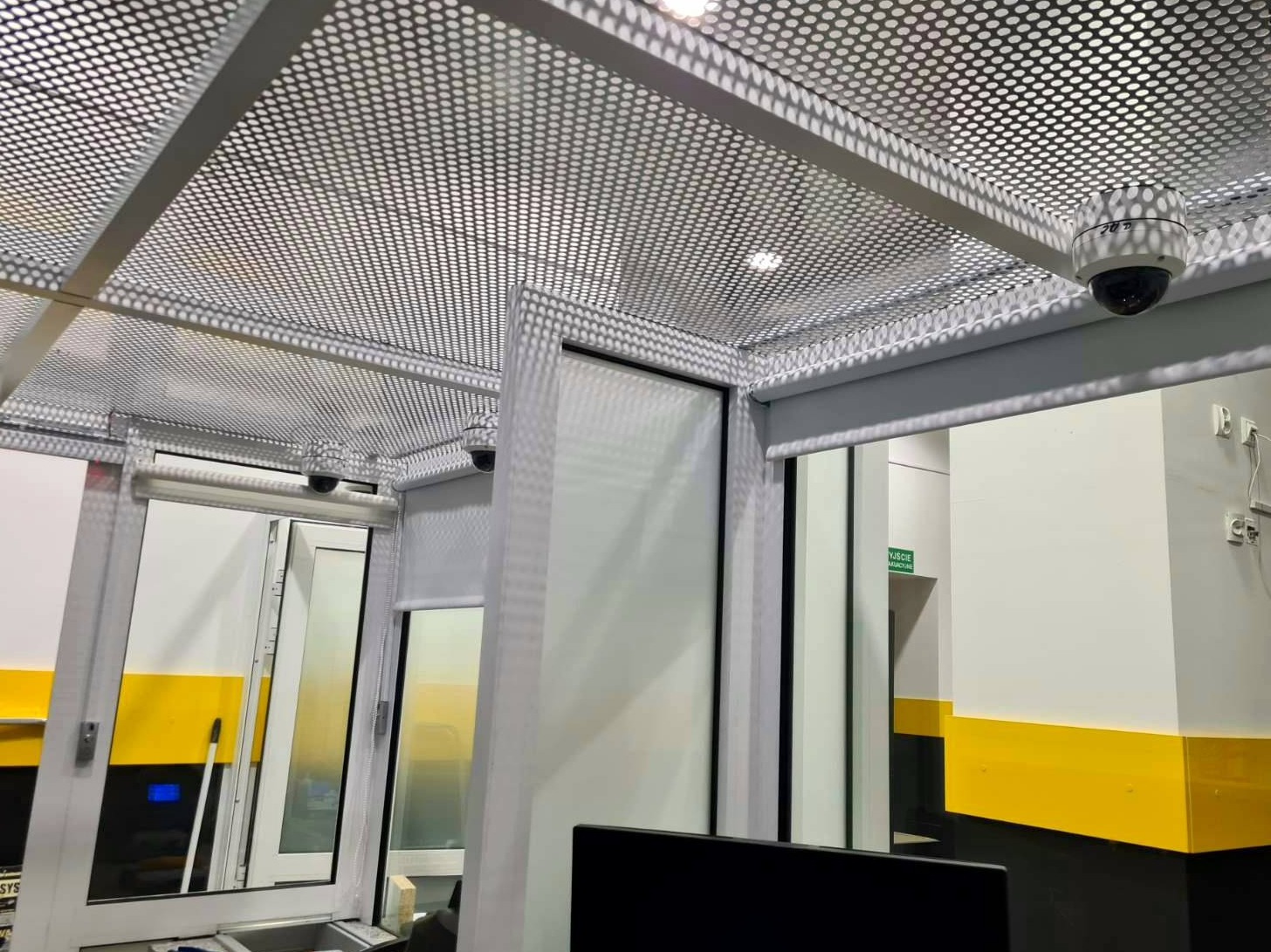 Kopułkowe kamery monitoringu pod perforowanym sufitem w biurze z żółtymi akcentami, widok z dołu.