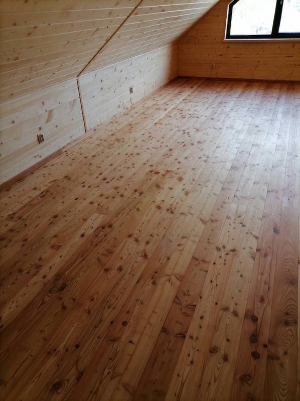 Poddasze wykończone boazerią i drewnianą podłogą z widocznymi sękami, okno dachowe w czarnej ramie.