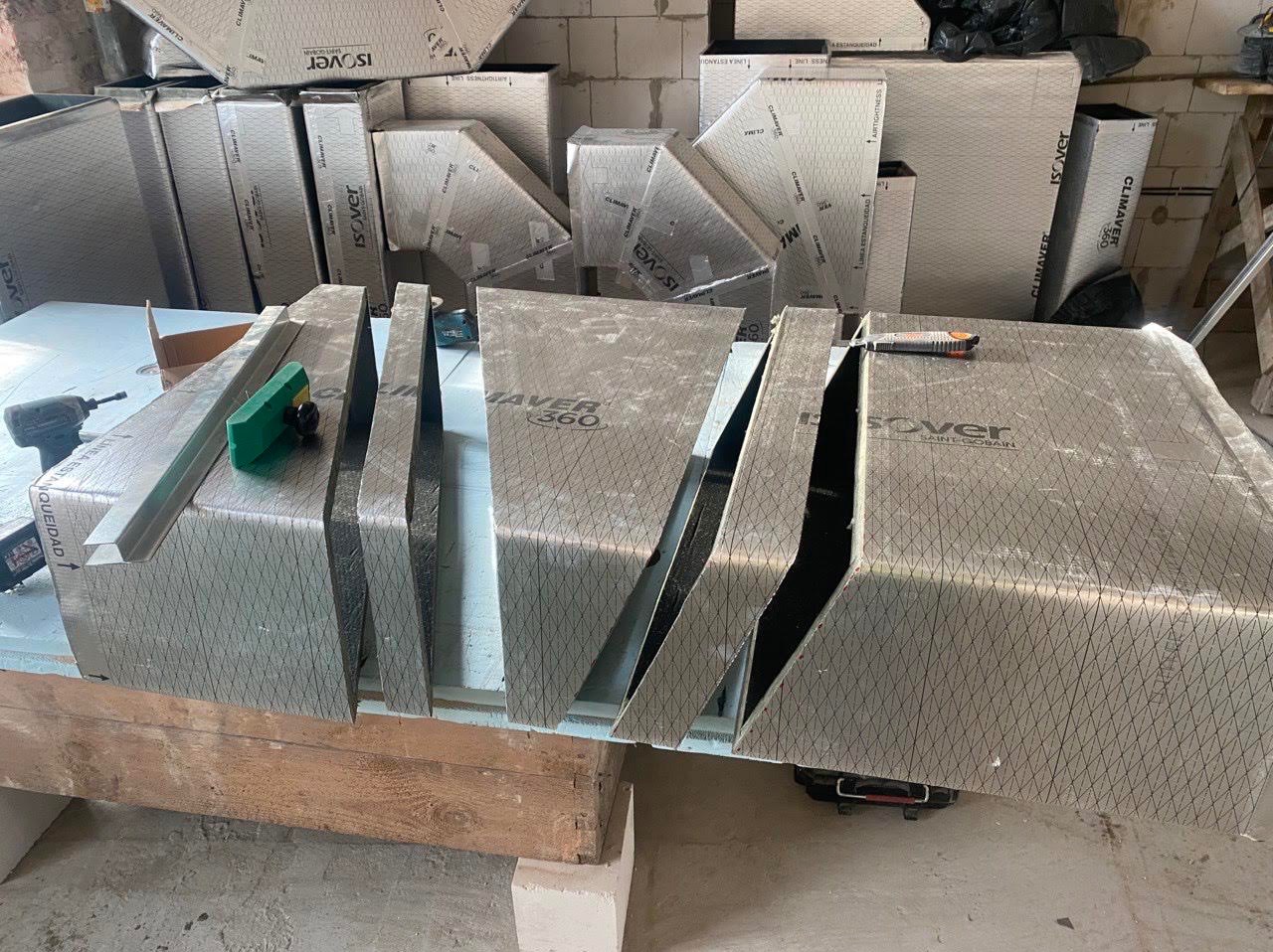 Przygotowane do montażu elementy izolacyjne Climaflex z widocznymi narzędziami: wkrętarka, nóż tapicerski i szczotka, na tle zapakowanych płyt izolacyjnych Isover.