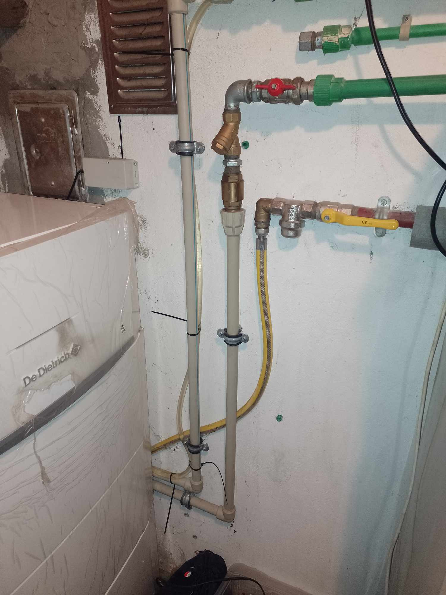 Instalacja grzewcza z kotłem De Dietrich, rurami z zaworami i przyłączem gazowym w pomieszczeniu technicznym o surowych ścianach.