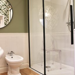 FARMA Styl Elżbieta Wieczorek - Nowoczesna łazienka z bidetem, kabiną prysznicową z czarnymi ramami i przezroczystym krzesłem. Lustro w okrągłej ramie z motywem roślinnym.