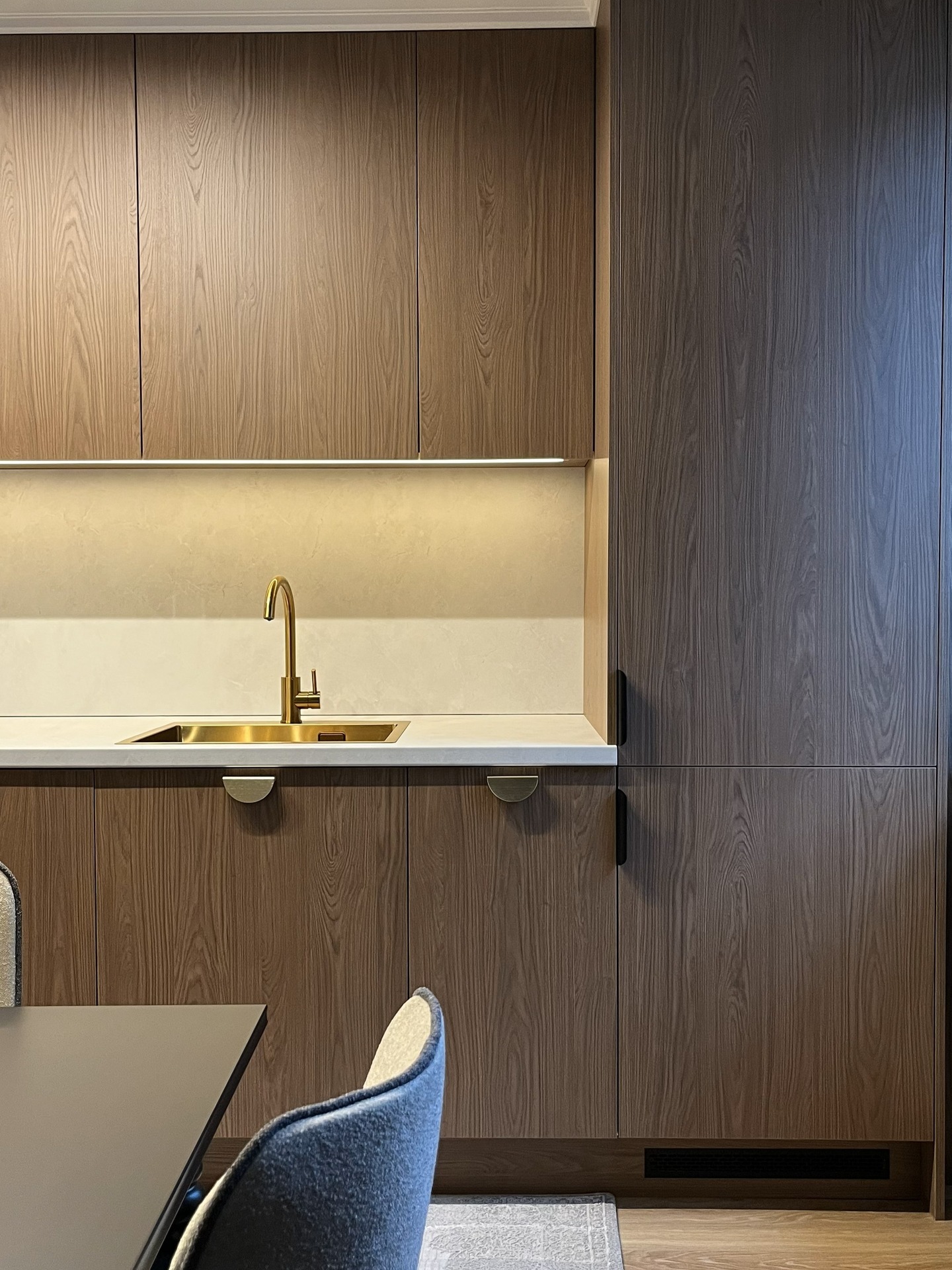 Nowoczesna zabudowa kuchenna z drewnianymi frontami, złotą armaturą i subtelnym oświetleniem LED. Minimalistyczny design z dbałością o detale.