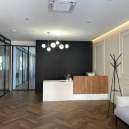 Nowoczesne wnętrze kancelarii prawnej z recepcją z drewnianym frontem, szklanymi ścianami działowymi i parkietem w jodełkę.