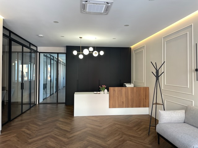 Nowoczesne wnętrze kancelarii prawnej z recepcją z drewnianym frontem, szklanymi ścianami działowymi i parkietem w jodełkę.