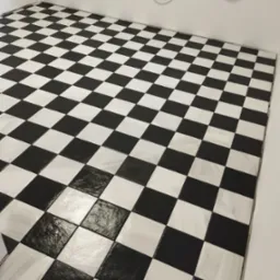 Ułożona podłoga z czarno-białych płytek w szachownicę, widoczne niedociągnięcia w fugach i instalacja elektryczna na ścianie.