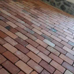 Podłoga wyłożona czerwoną cegłą w pomieszczeniu z fragmentem ściany wykończonej kamieniem w Trzciance.