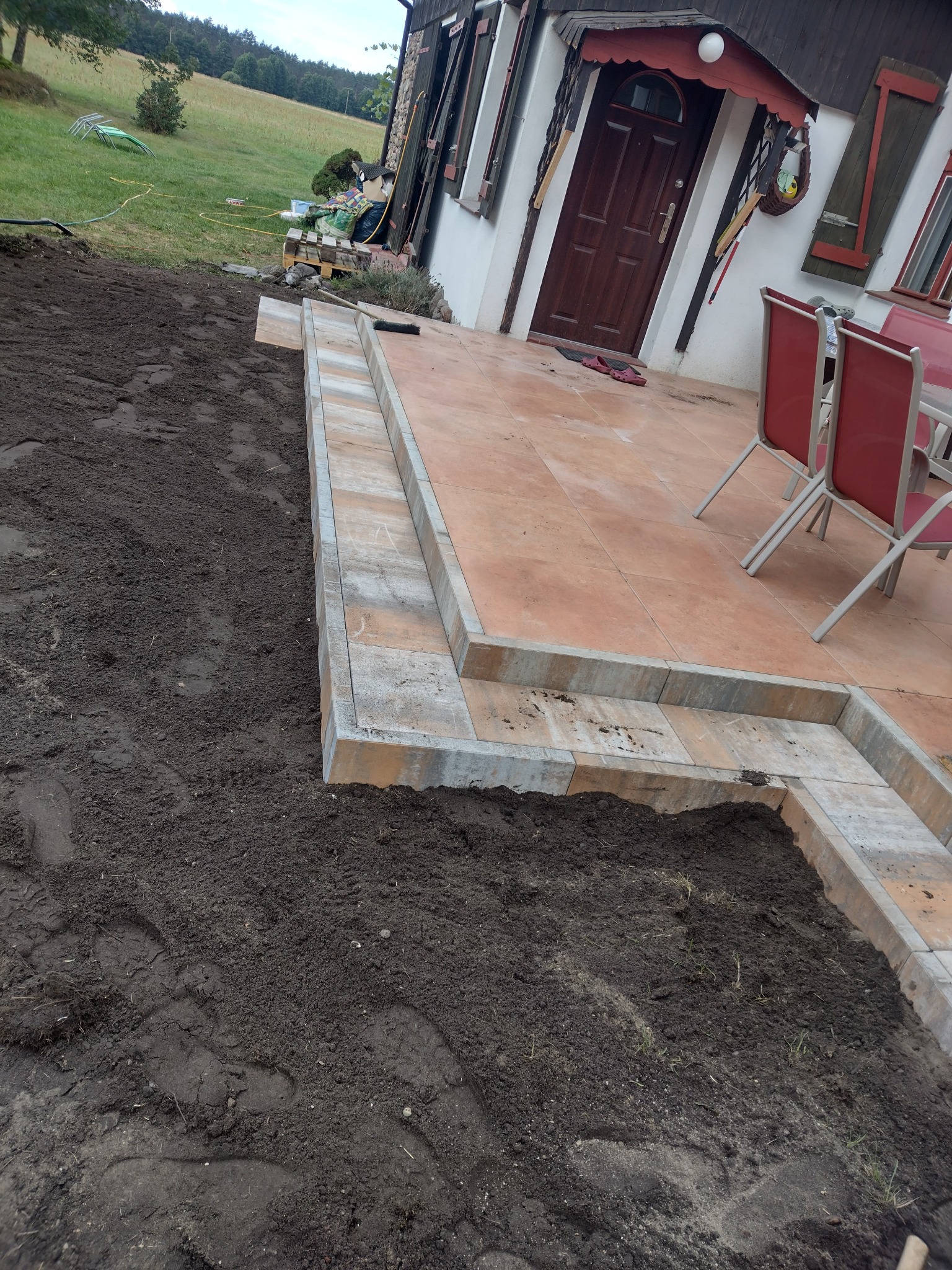 Ułożona kostka brukowa obramowująca taras z płytek ceramicznych, widoczny fragment przygotowanego terenu pod dalsze prace ziemne.