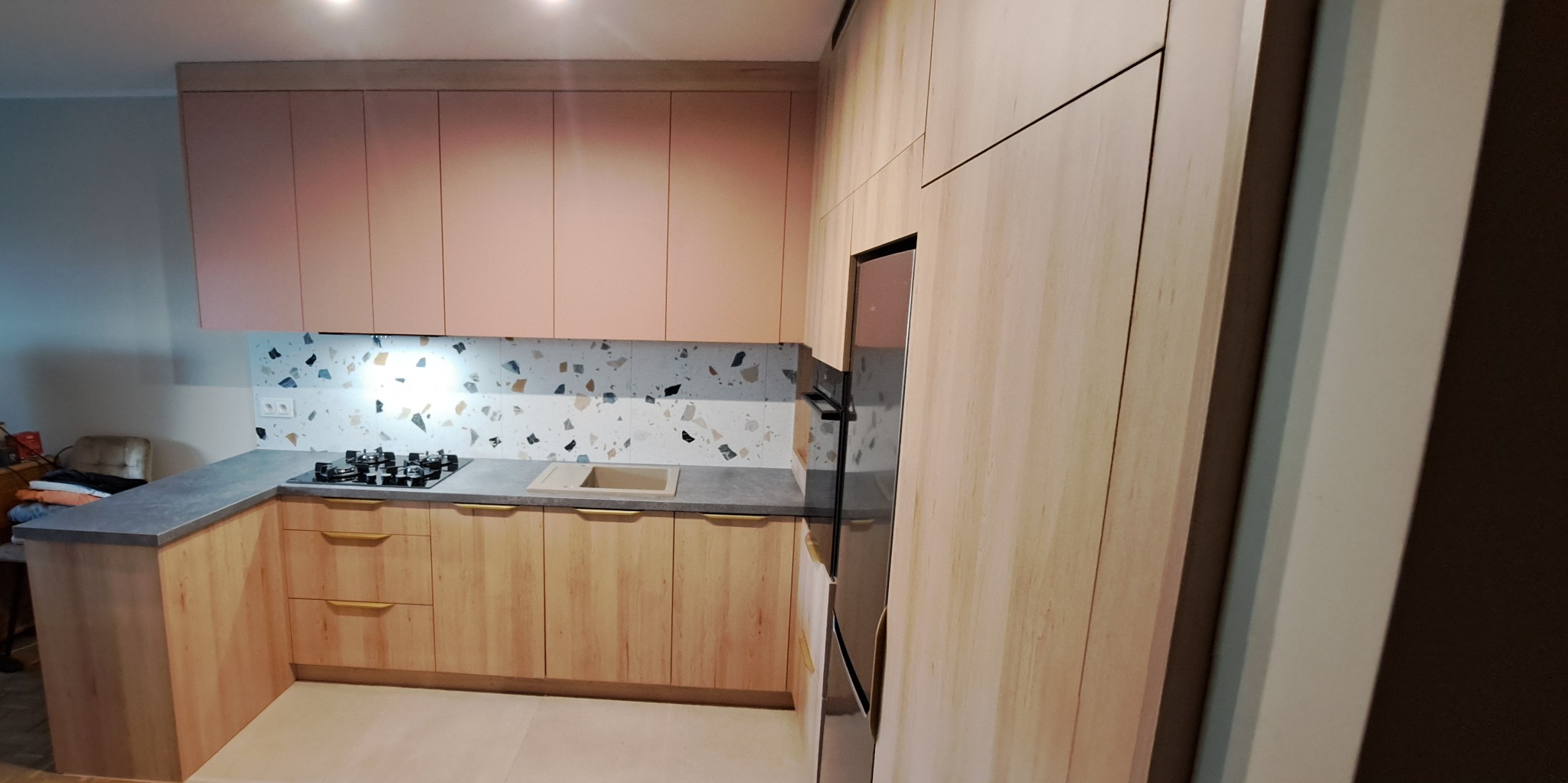 Jasna kuchnia na wymiar z różowymi górnymi szafkami, blatem z szarego konglomeratu i mozaiką nad blatem.