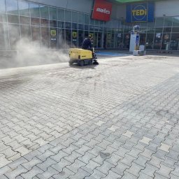Z POŁYSKIEM Bartłomiej Zienkiewicz - Operator na maszynie Kärcher czyści kostkę brukową przed sklepem Martes i Tedi. Widoczna para wodna unosząca się znad czyszczonej powierzchni.