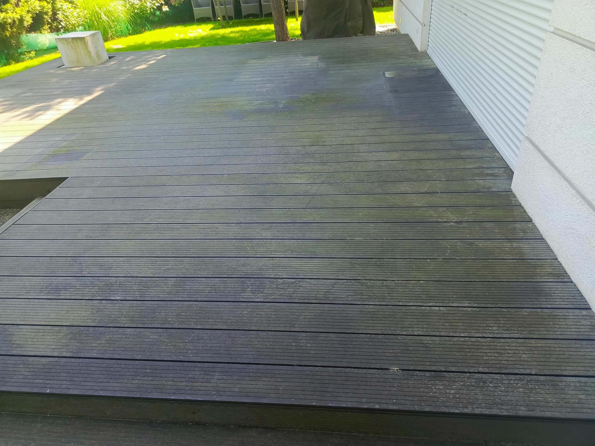 Zewnętrzny taras z desek kompozytowych, widoczne zabrudzenia i porosty, zarys budynku w tle.