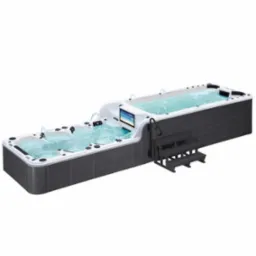 Długi basen spa z hydromasażem i przeciwprądem, wbudowany telewizor, zewnętrzna obudowa w kolorze grafitowym, schodki wejściowe.