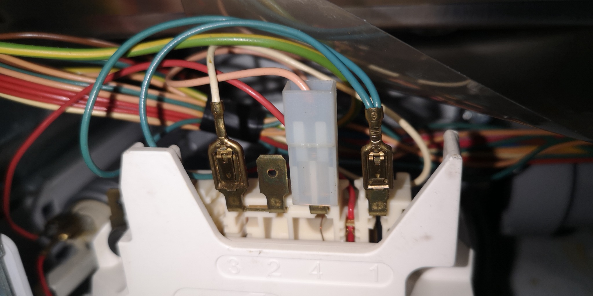 Szczegółowe ujęcie z wnętrza urządzenia AGD, prezentujące podłączenie przewodów elektrycznych do białej listwy z numeracją, z widocznymi metalowymi konektorami i plastikową kostką.