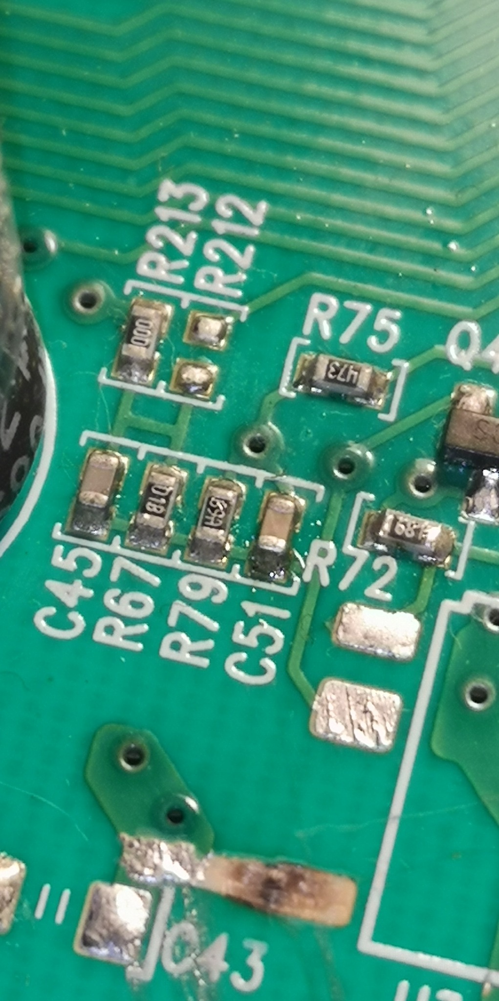 Zbliżenie na zieloną płytę drukowaną z przylutowanymi elementami elektronicznymi, widoczne oznaczenia R213, R75, C45, R67, R79, C51, R72, ślady topnika i przypalenia w dolnej części.