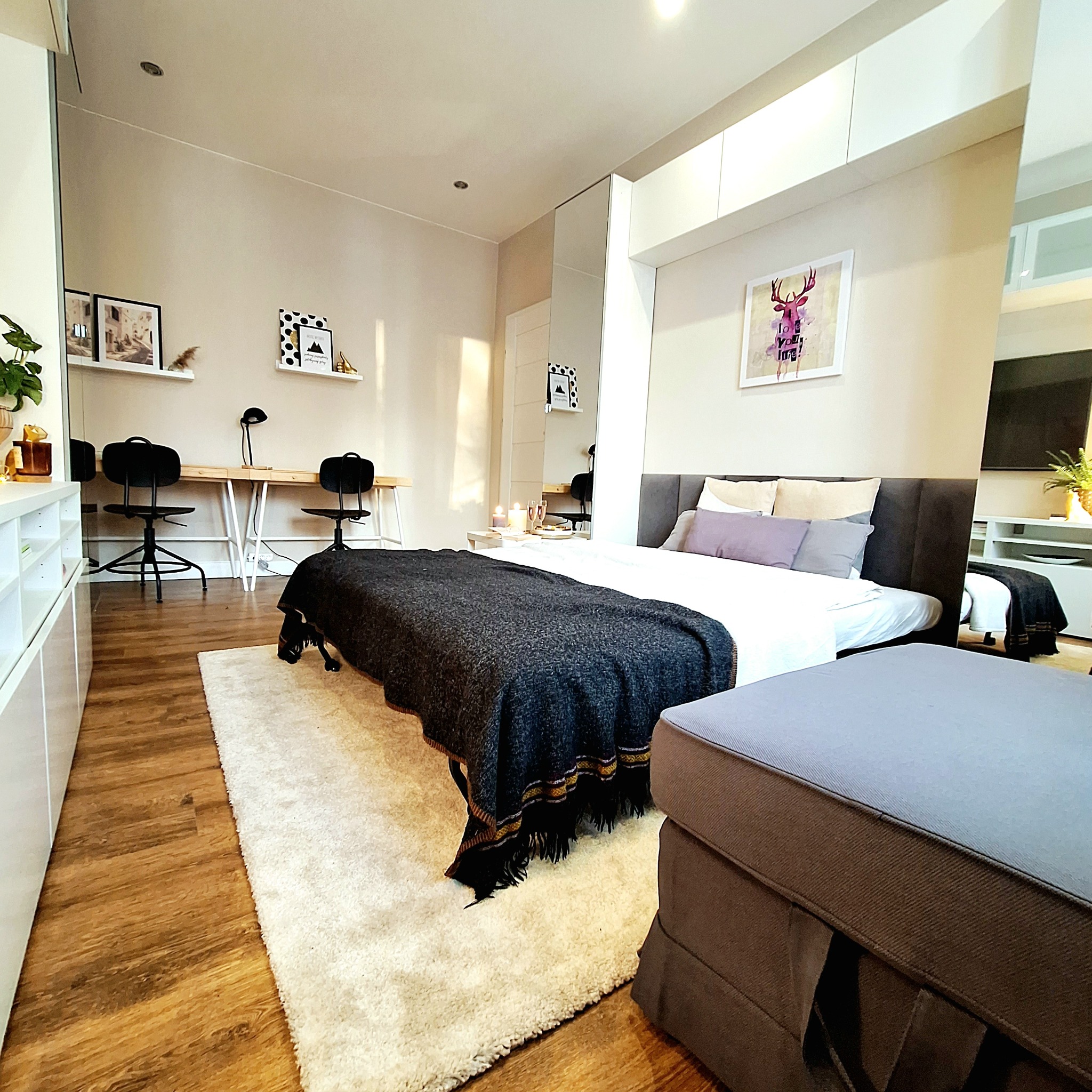 Nowoczesna sypialnia z drewnianą podłogą, białymi meblami, łóżkiem z szarym wezgłowiem i biurkiem z krzesłami w tle.