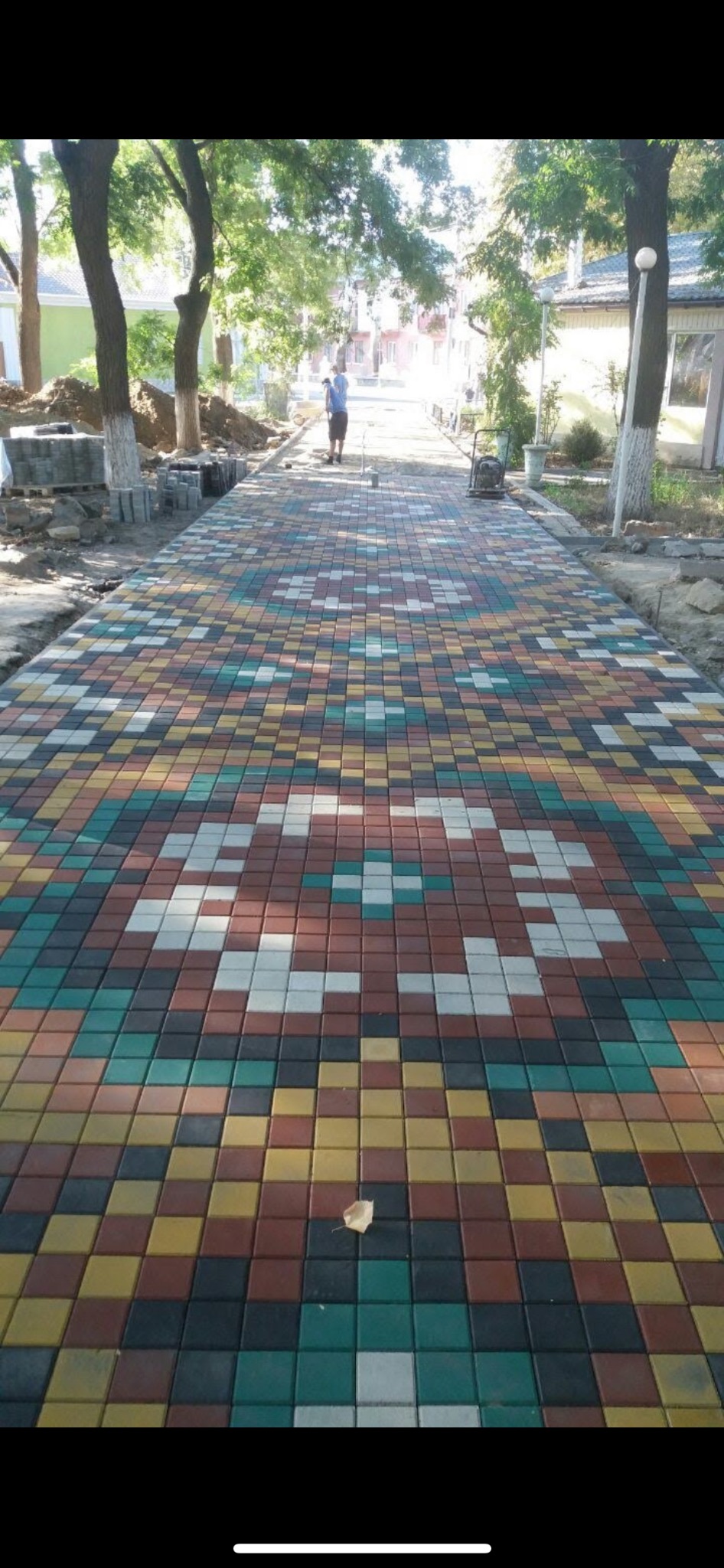 Kolorowa aleja z kostki brukowej ułożonej we wzór, w tle widoczna osoba i maszyna budowlana.